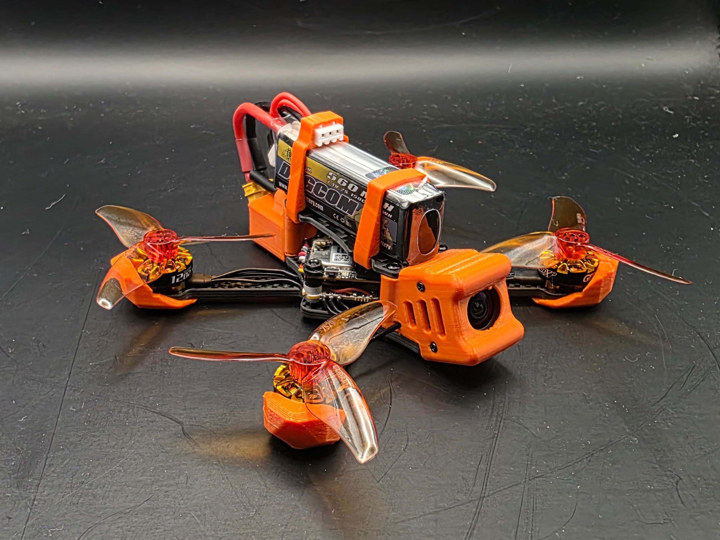 Kompletně postavený quadcopter na rámu Minibyte 2.5 s oranžovými TPU díly, namontovanou FPV kamerou, vrtulemi a baterií Dogcom 560 mAh 2S.