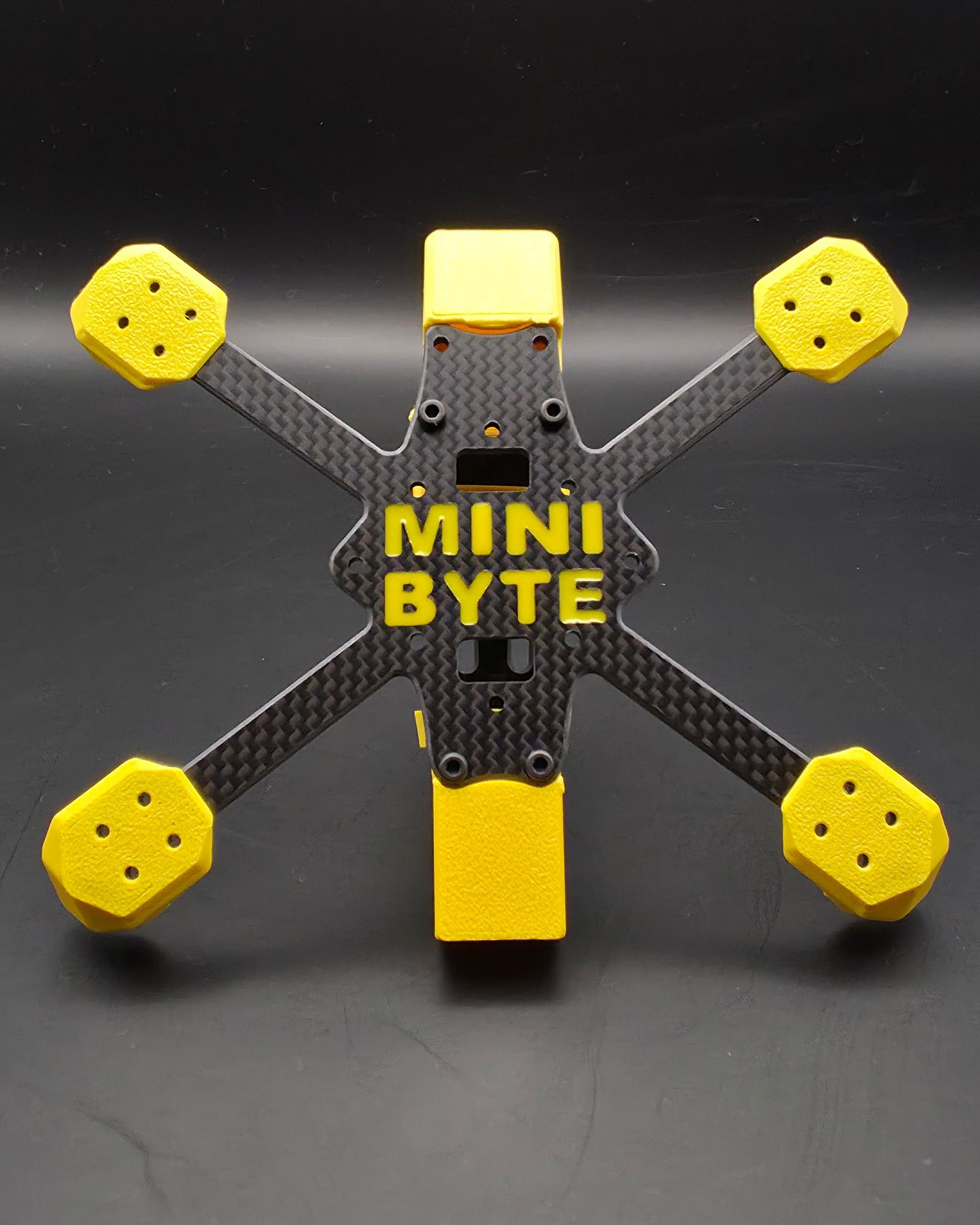 Rám Minibyte 2.5 zespodu: karbonová deska se žlutým potiskem MINIBYTE a osmihrannými TPU chrániči u úchytů motorů.